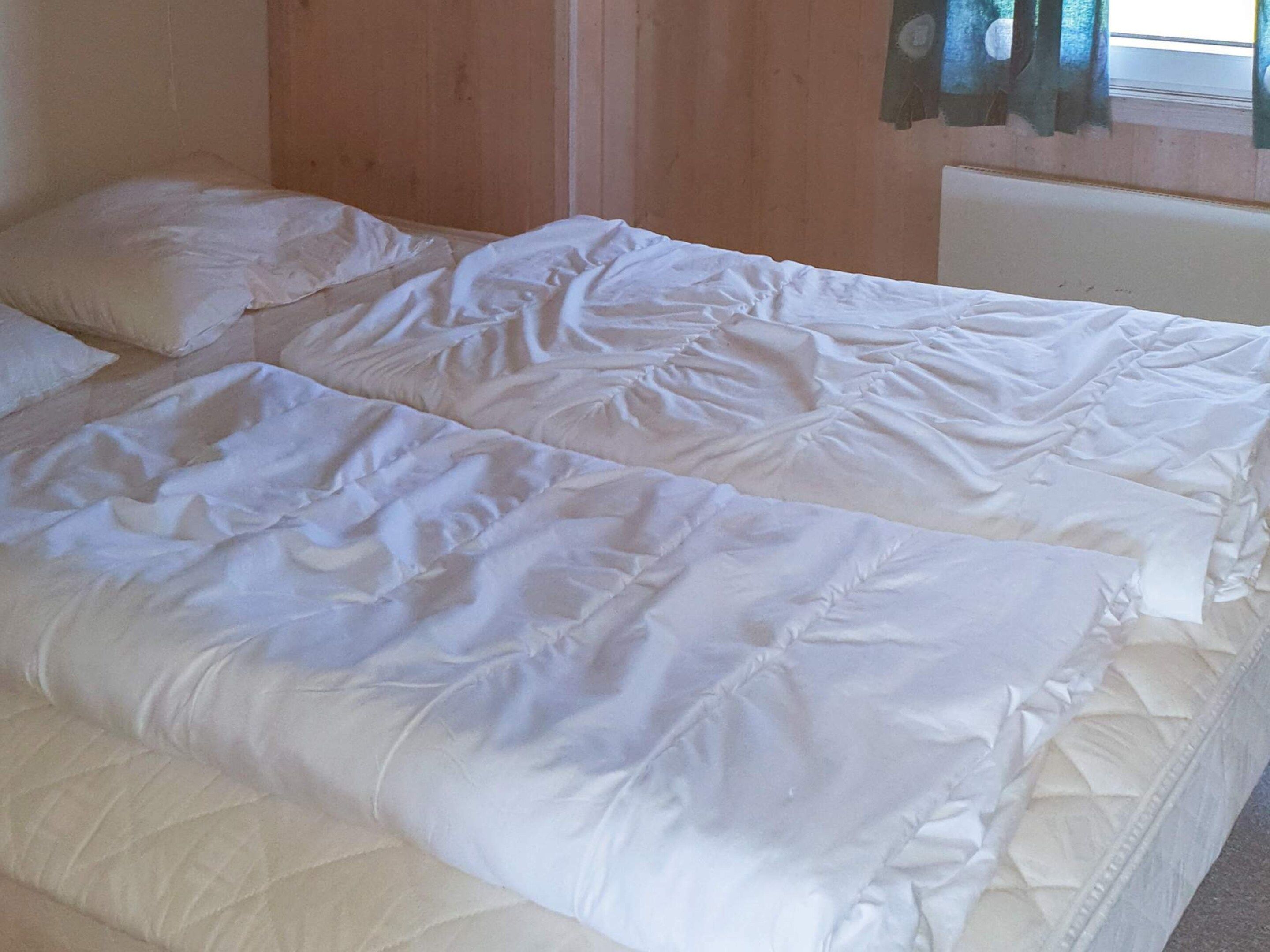 A double bed with white bedding in a room with wooden walls and a window with curtains.