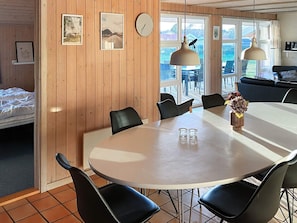 A dining area with a round table, black chairs, and a vase with flowers. There are framed pictures on the wall and a clock. - 4 Star Holiday Home in Nordborg (Nordborg)