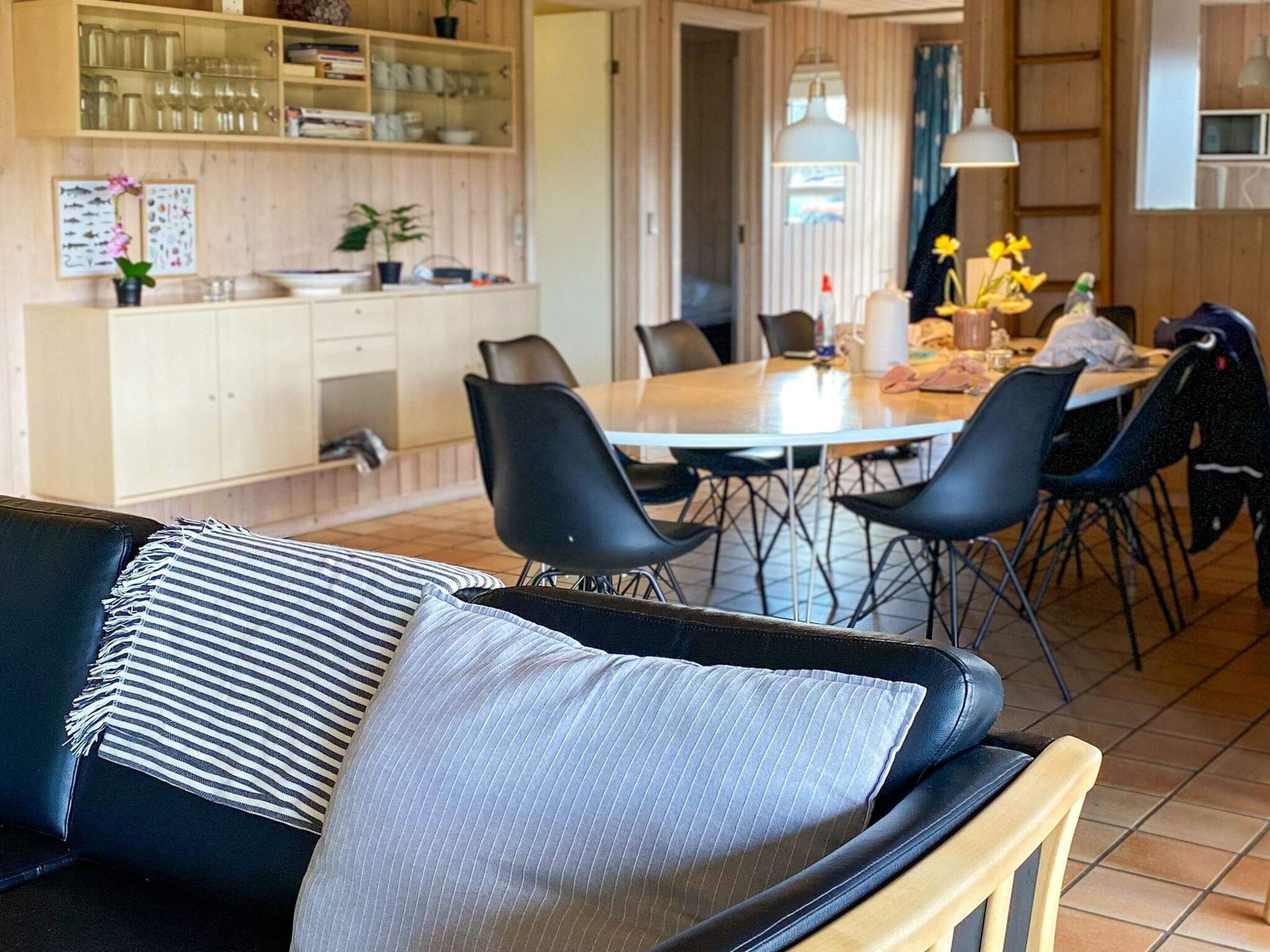 Ett modernt vardagsrum med en svart lädersoffa, en randig kudde och en trästol.