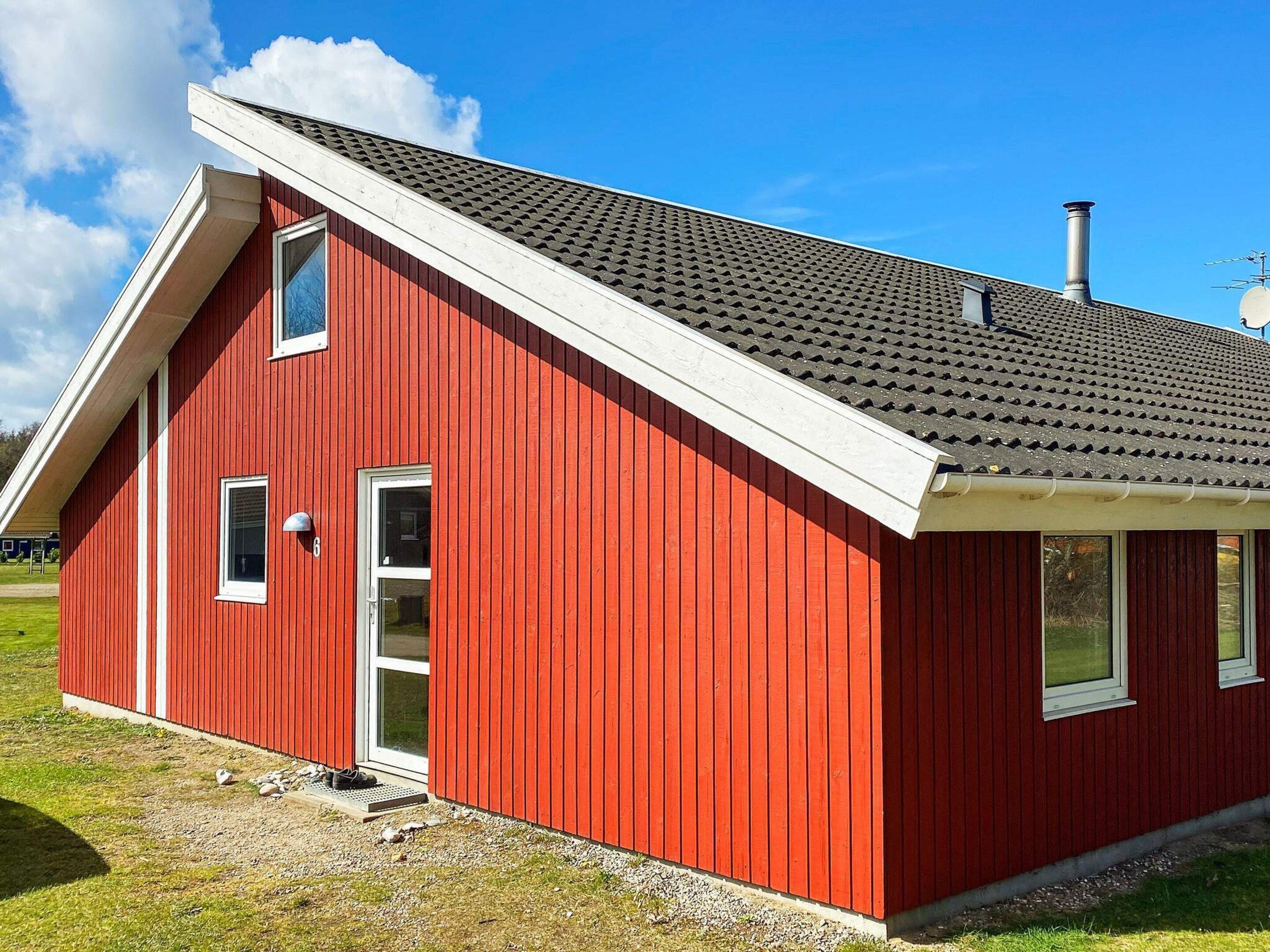 A red building with a sloped roof, a chimney, and a small porch area.