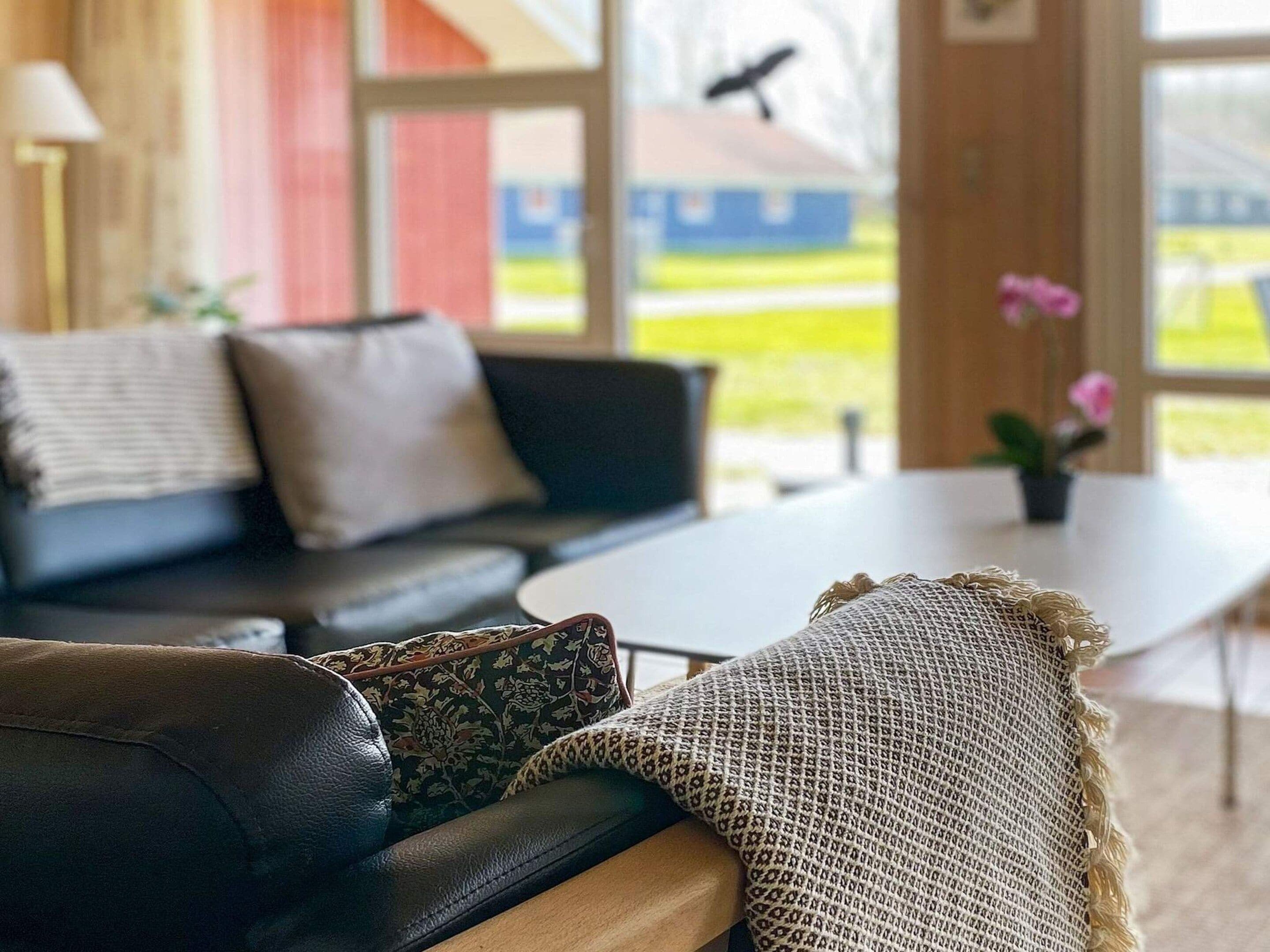 A modern living room with a black leather sofa, a round coffee table, and a large window offering a view of the outdoors.