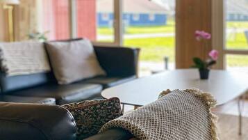 A modern living room with a black leather sofa, a round coffee table, and a large window offering a view of the outdoors.