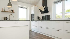 A modern kitchen with white cabinets, a wooden countertop, and a large window. - Holiday Home in Juelsminde (Horsens)