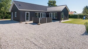 A modern building with a gravel driveway, a fenced area, and a clear sky. - Holiday Home in Juelsminde (Horsens)