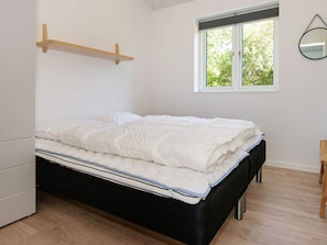 A bedroom with a bed, a window, a bedside table, and a hanging mirror.