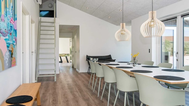 A modern dining area with a long table, multiple chairs, and pendant lights. - Holiday Home in Juelsminde (Horsens)