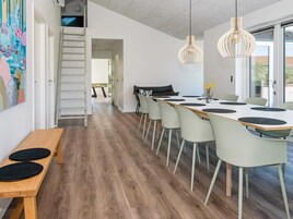 Et moderne spiseområde med et langt bord, flere stole og hængende lamper.