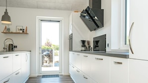 A modern kitchen with white cabinets, a built-in oven, and a coffee maker. - Holiday Home in Juelsminde (Horsens)