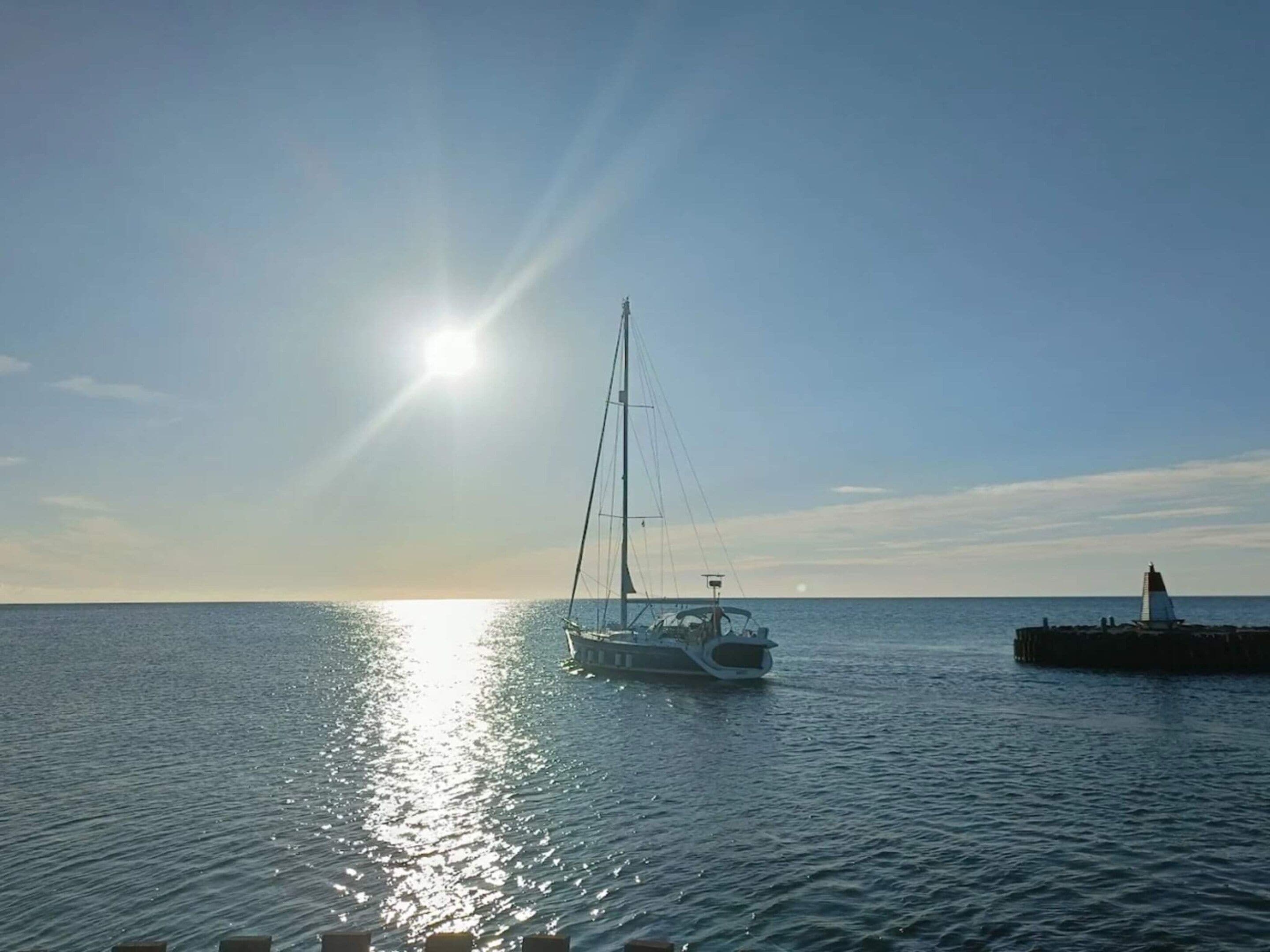 A calm sea with a sailboat and a lighthouse in the distance.