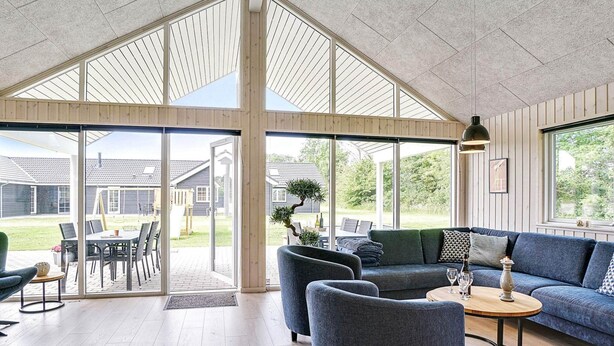 A spacious living area with a large glass door leading to an outdoor patio, a blue sofa, and a round coffee table. - Holiday Home in Grenaa (Grenaa)
