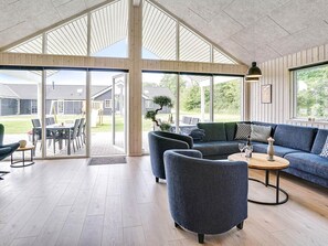 Un vaste espace de vie avec une grande porte-fenêtre donnant sur une terrasse extérieure, un canapé bleu et une table basse ronde.