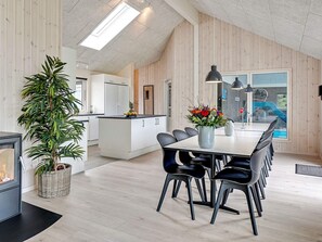 A modern kitchen with a central island, dining area with chairs, a large potted plant, and a view of a swimming pool. - Holiday Home in Grenaa (Grenaa)