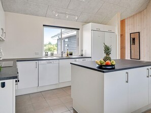 A modern kitchen with white cabinetry, a built-in dishwasher, and a large island with a fruit bowl.