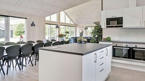 A modern kitchen with white cabinetry, a large island, and built-in appliances. - Holiday Home in Grenaa (Grenaa)