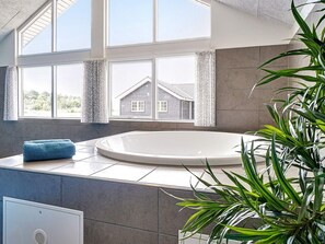 A modern bathroom with a large bathtub, a window with curtains, and a potted plant. - Holiday Home in Grenaa (Grenaa)