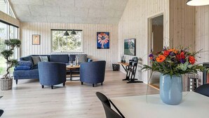 A modern living room with a sofa, chairs, a dining table, and a large window. - Holiday Home in Grenaa (Grenaa)