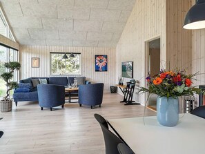 A modern living room with a sofa, chairs, a dining table, and a large window. - Holiday Home in Grenaa (Grenaa)