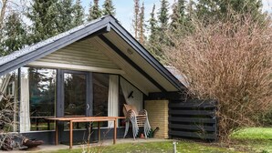 A modern house with a glass door entrance, a wooden table outside, and a garden with flowers and a pond. - 6 Person Holiday Home in Ebeltoft (Ebeltoft)