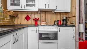 A kitchen with white cabinets, a stove, and an oven. There is a red kettle and a coffee maker on the counter. - 6 Person Holiday Home in Ebeltoft (Ebeltoft)