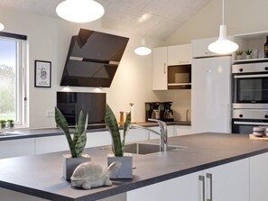 A modern kitchen with a central island, pendant lighting, and built-in appliances. - Holiday Home in Idestrup (Idestrup)