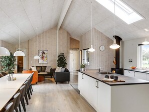 A modern kitchen with a large island, pendant lighting, and a visible clock. - Holiday Home in Idestrup (Idestrup)