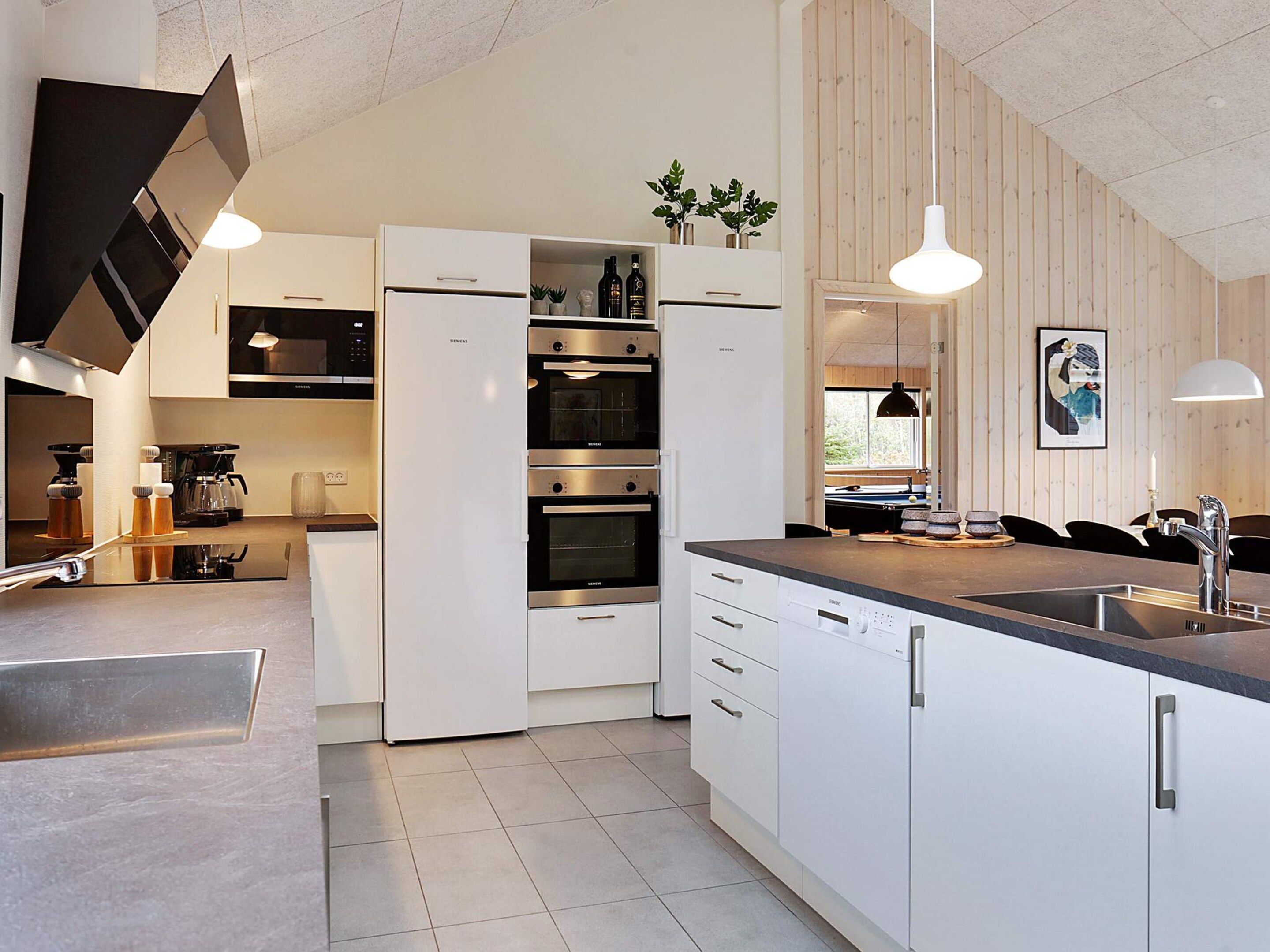 A modern kitchen with white cabinetry, stainless steel appliances, and pendant lighting.