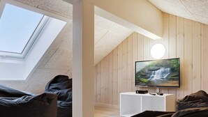 Ein Loft-Zimmer mit Dachfenster, einem Fernseher auf einem weißen Standfuß und schwarzen Sitzsäcken.