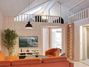 Habitación estilo loft con techo alto, paredes de madera, televisor, sofá, planta y una escalera.