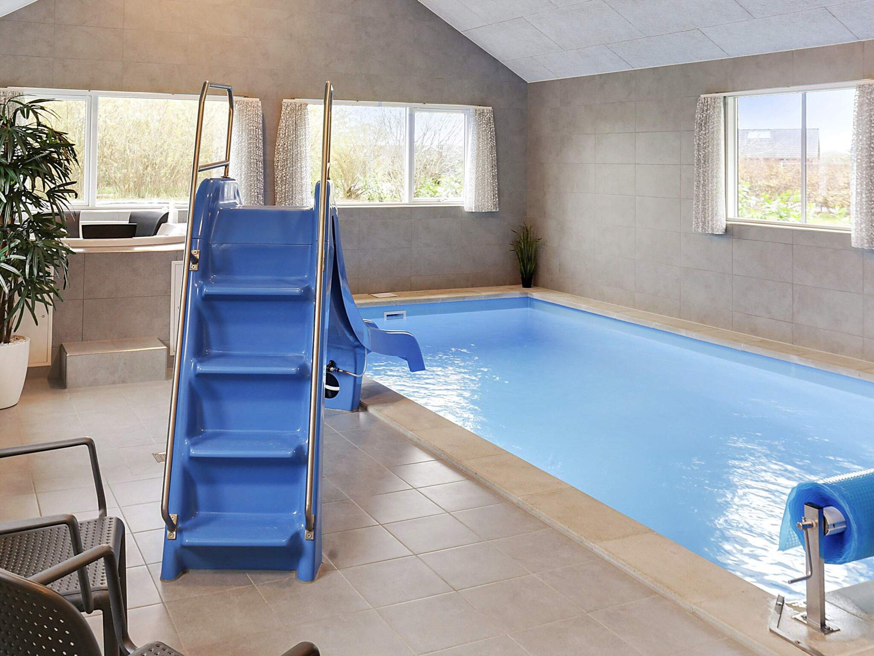 An indoor swimming pool with a blue slide, a reception desk, and windows with curtains.