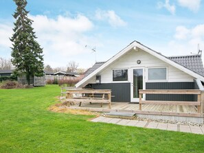 A single-story house with a sloped roof, a front door, and a small deck area with benches.
