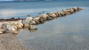 A rocky shoreline with a calm sea and a distant landmass. - 5 Person Holiday Home in Hejls (Hejls)
