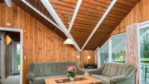 A cozy living room with wooden walls, a wooden ceiling, a glass coffee table, and two grey sofas. - 5 Person Holiday Home in Hejls (Hejls)