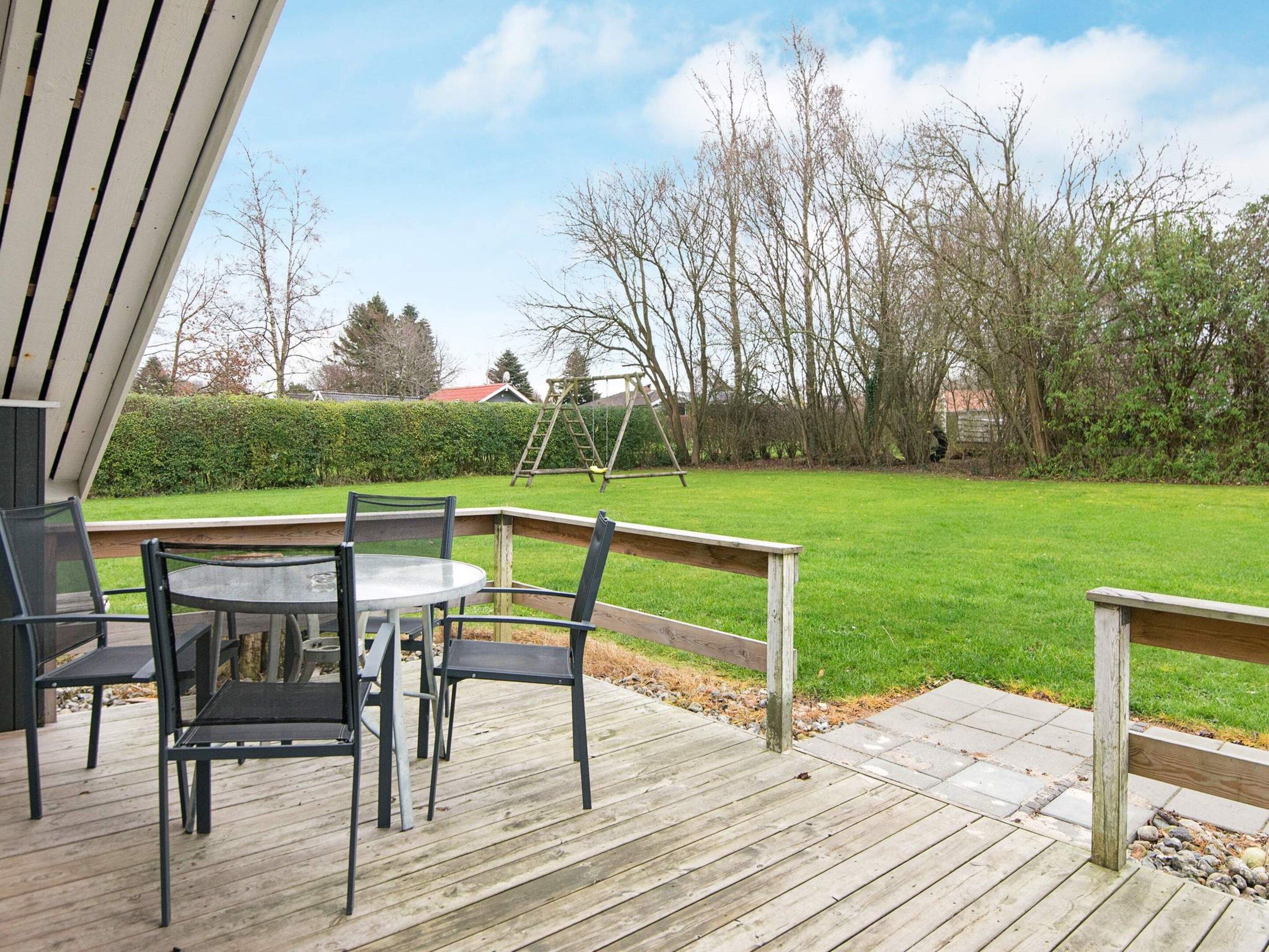 An outdoor deck with a table and chairs, a wooden swing set, and a grassy yard.