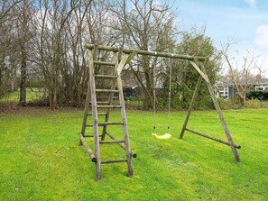 A wooden swing set with a ladder in a grassy yard.