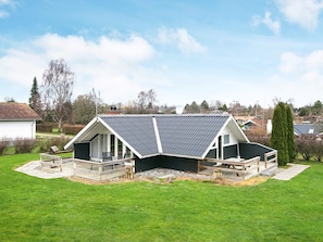 A house with a sloped roof, a deck, and a large lawn. - 5 Person Holiday Home in Hejls (Hejls)