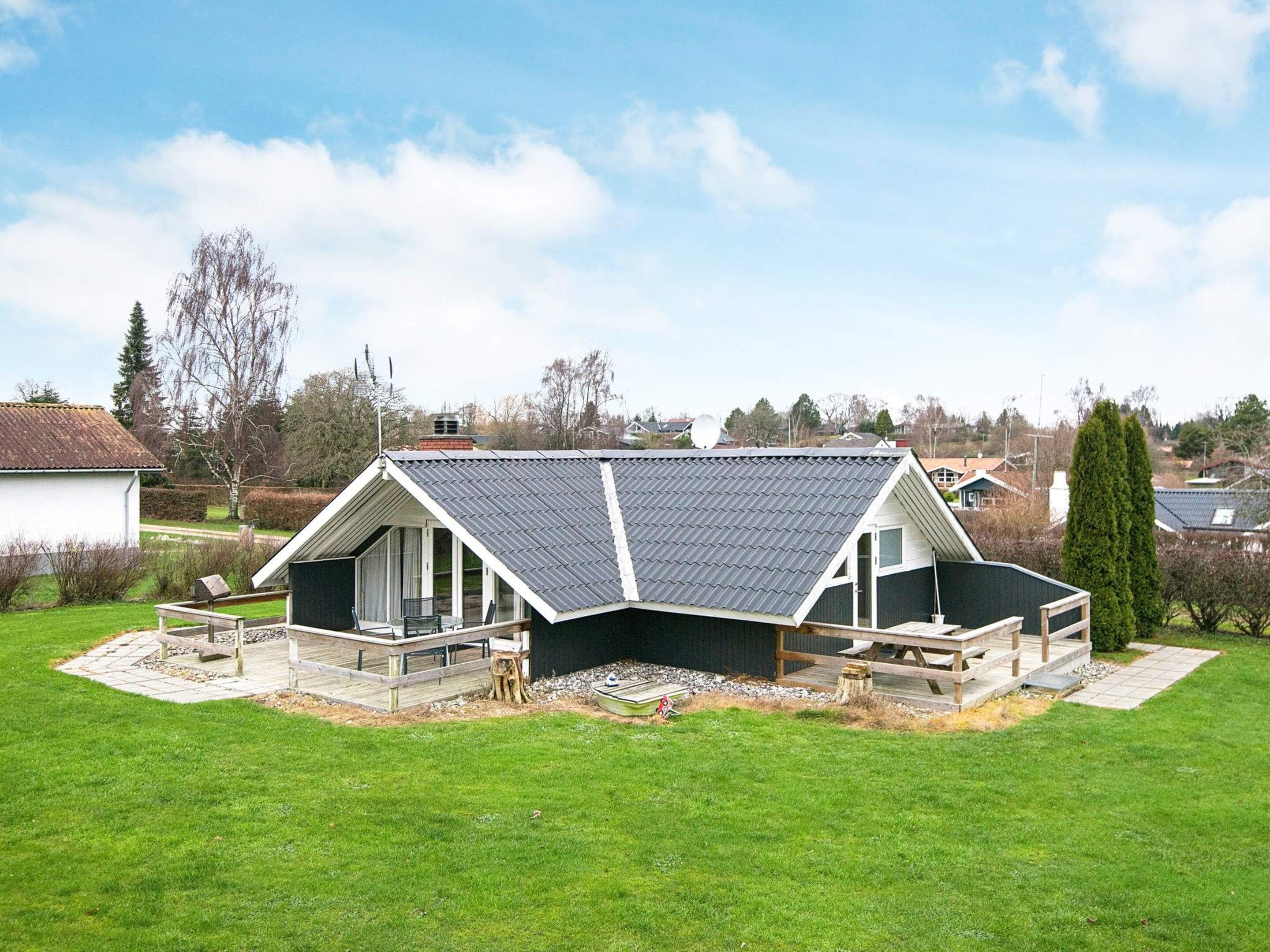 Ein Haus mit geneigtem Dach, einer Terrasse und einem Rasen.