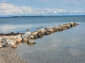 A rocky shoreline with a calm sea and a distant landmass. - 5 Person Holiday Home in Hejls (Hejls)