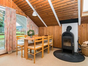 A cozy room with a wooden ceiling, a fireplace, a dining table with chairs, and a large window with curtains. - 5 Person Holiday Home in Hejls (Hejls)