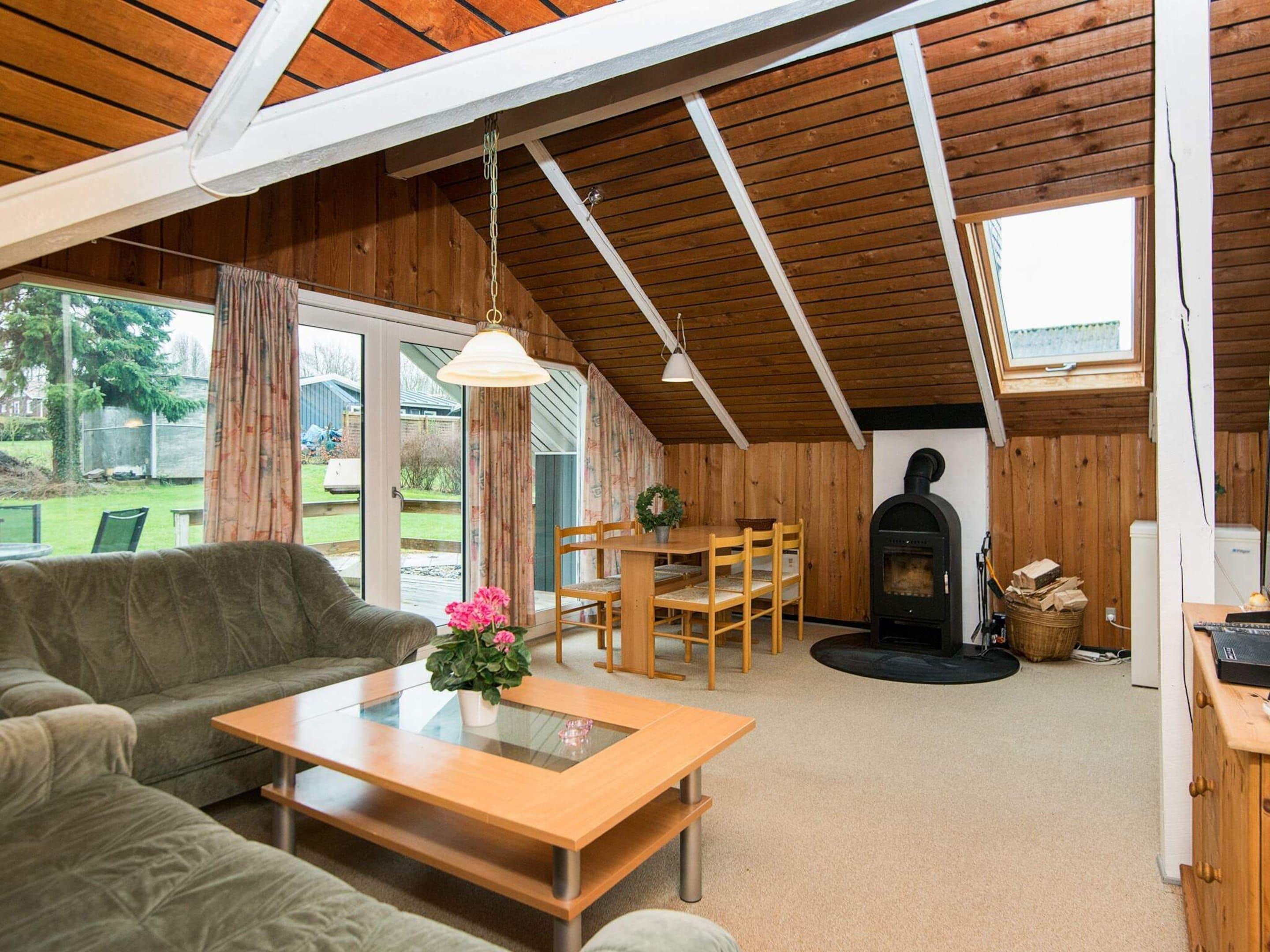 Una sala de estar acogedora con un sofá, una mesa de centro de madera y un comedor con sillas. Se observa una chimenea al fondo.
