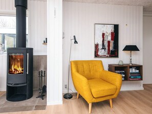 A room with a wood-burning stove, a yellow armchair, a bookshelf, and a painting on the wall. - 6 Person Holiday Home in Ringkobing (Ringkobing)