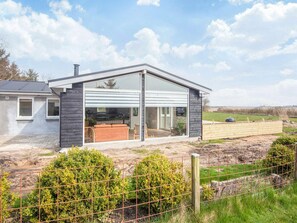 A modern house with a large glass sliding door, a fenced yard, and a view of the countryside. - 6 Person Holiday Home in Ringkobing (Ringkobing)