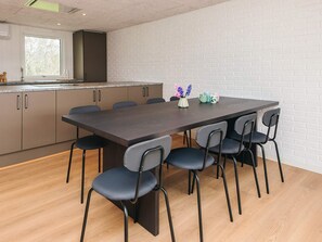 A modern kitchen with a large dining table and chairs, a white brick wall, and a window with a view of trees.