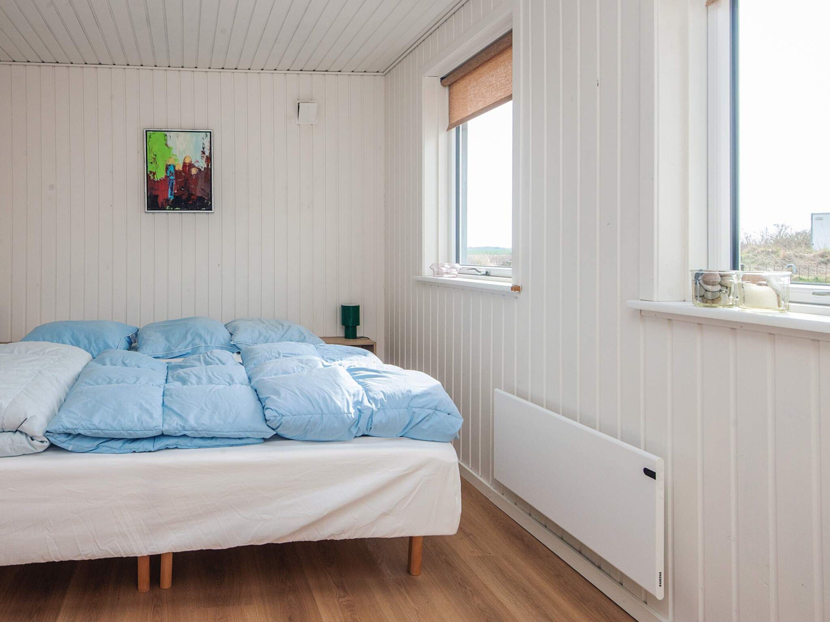 A bedroom with a bed, a window with a view, a radiator, and a small table with a lamp.