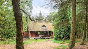 A rustic cabin with a thatched roof, surrounded by dense forest. - 6 Person Holiday Home in Blavand (Blavand)