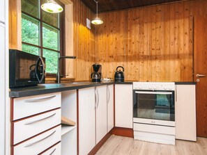 A compact kitchen with wooden walls, a white stove, and a kettle on the counter. - 6 Person Holiday Home in Blavand (Blavand)