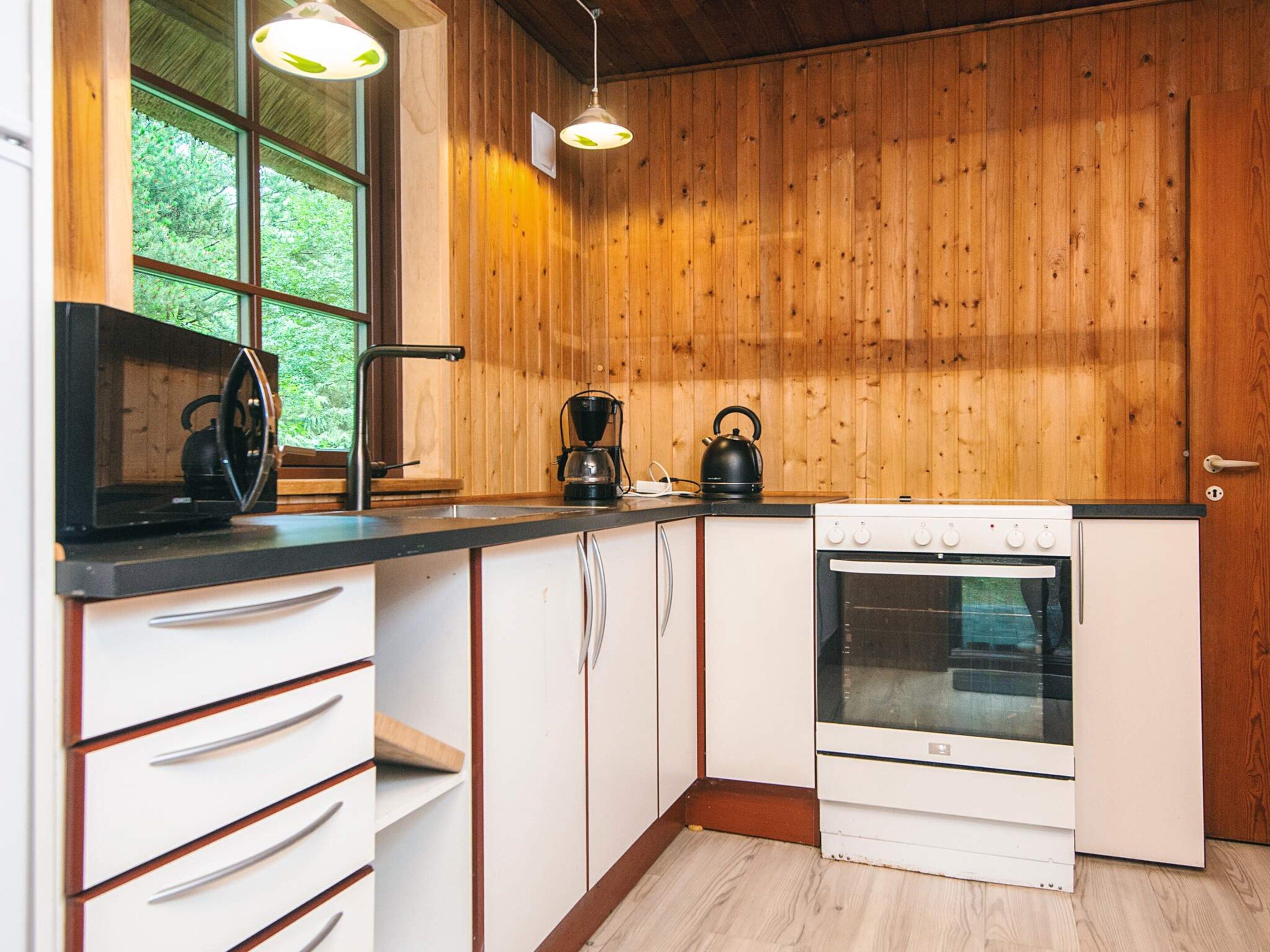 A compact kitchen with wooden paneling, a stove, a kettle, and a coffee maker.