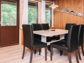 A dining area with a wooden interior, a white table, black chairs, and a pendant light. - 6 Person Holiday Home in Blavand (Blavand)