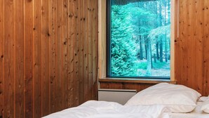 A bedroom with wooden walls, a bed with white bedding, and a window with a forest view. - 6 Person Holiday Home in Blavand (Blavand)