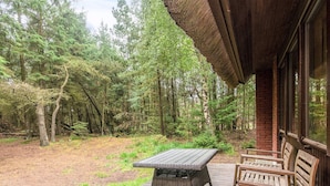 A wooden deck with a wicker table and two wooden chairs, overlooking a forested area. - 6 Person Holiday Home in Blavand (Blavand)