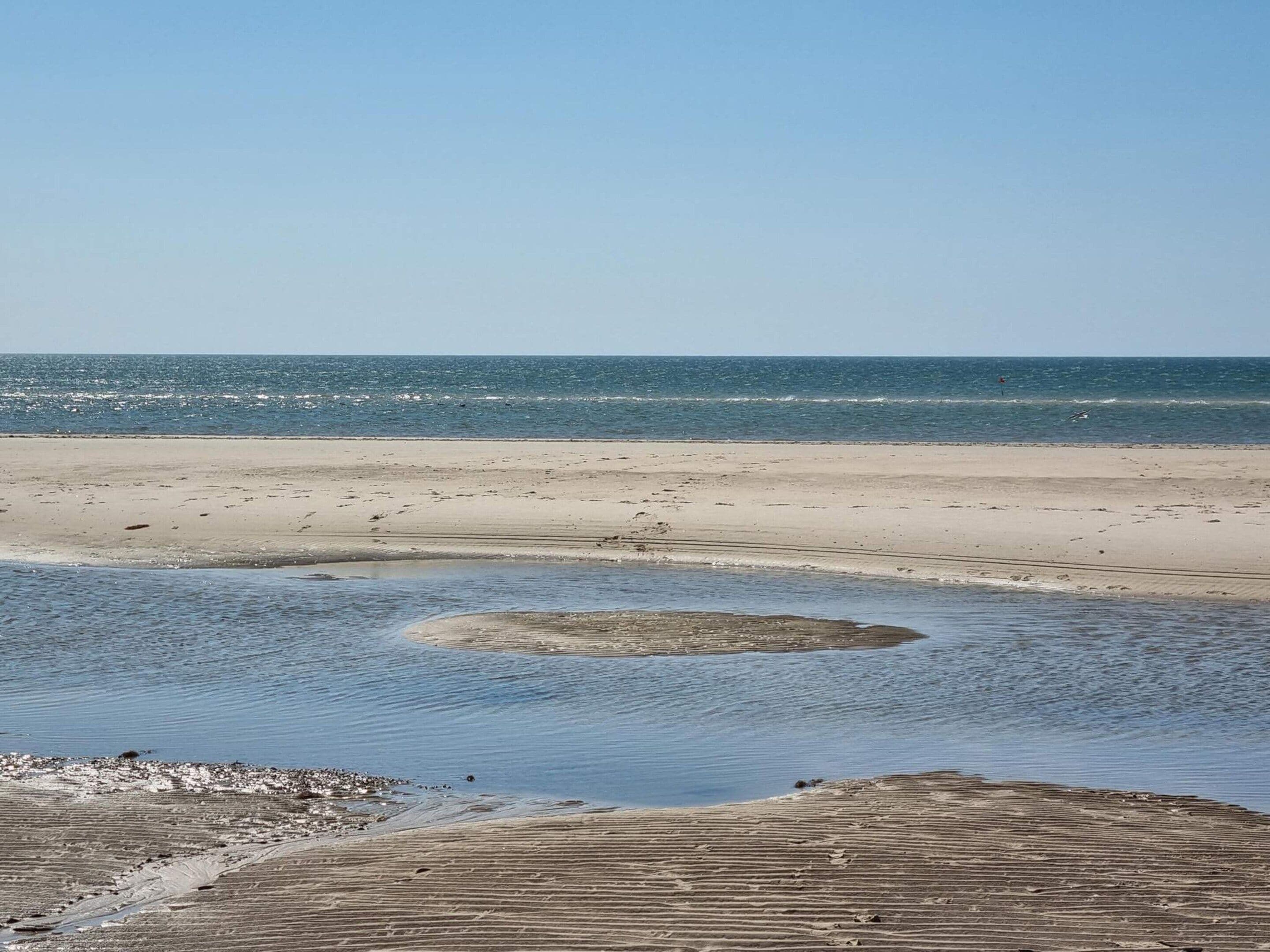 Une plage avec un ciel dégagé, une mer calme et un rivage sablonneux.